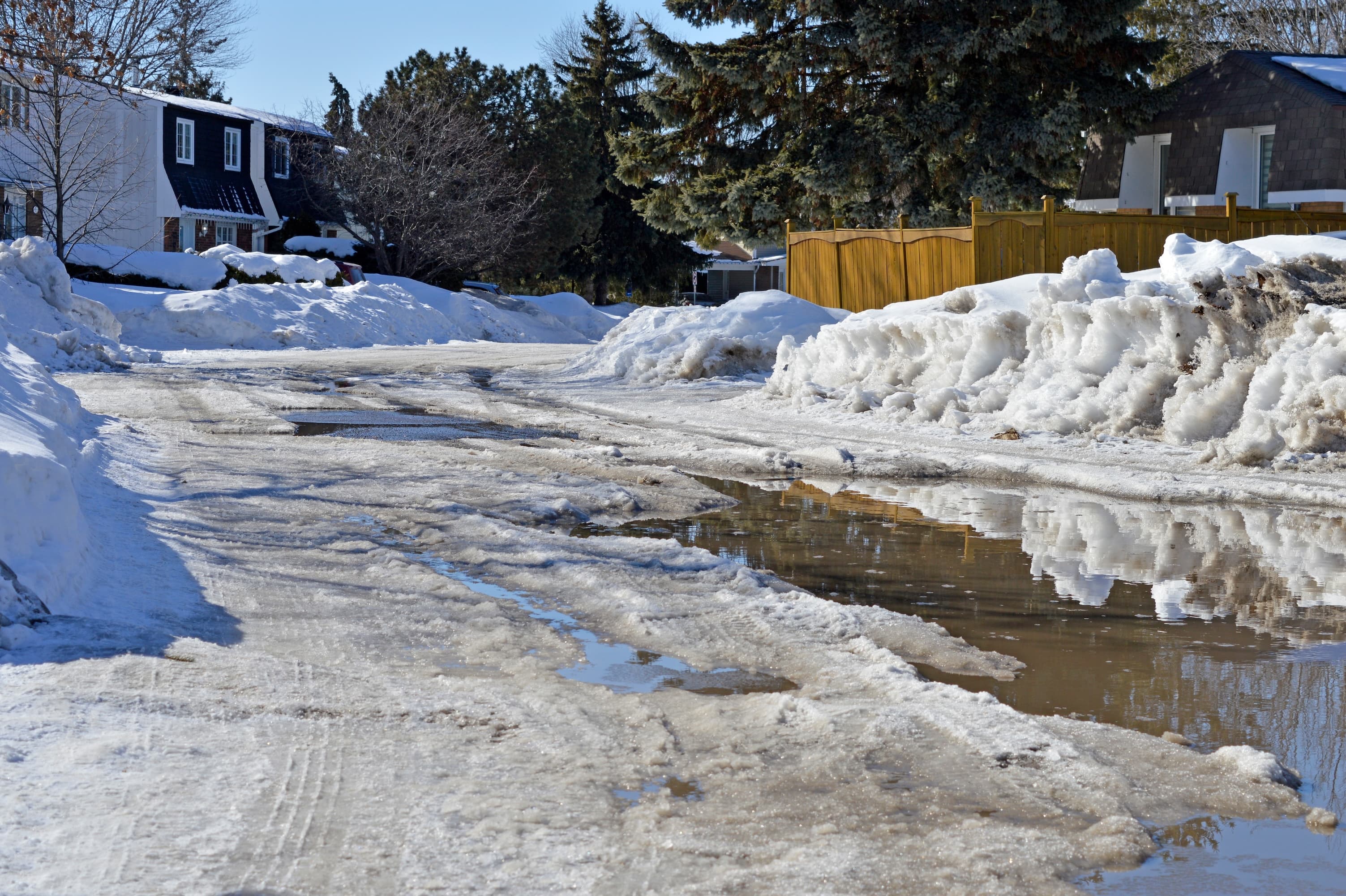 Residential street with melting snow and puddles.