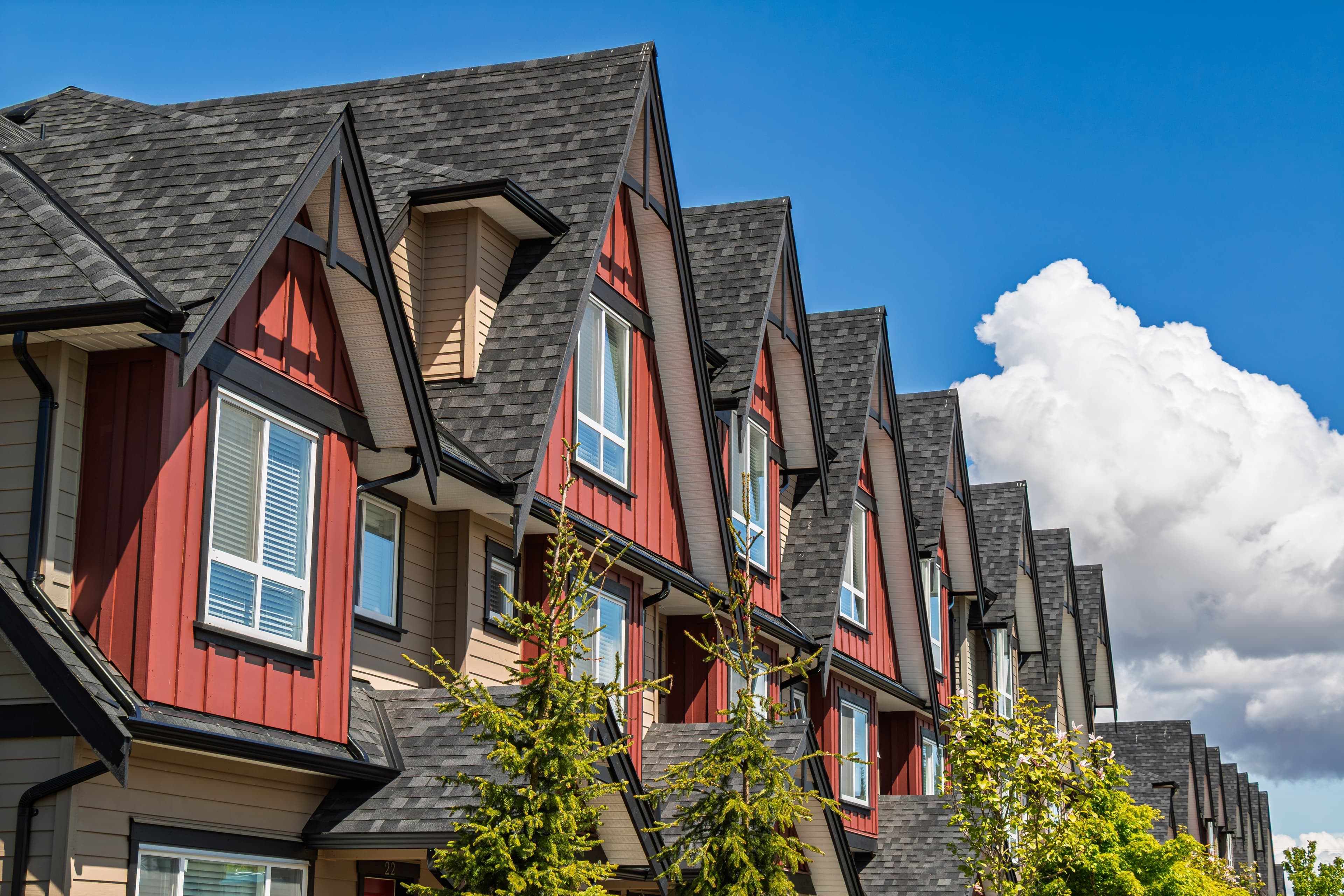Modern townhouses with steep roofs against a blue sky with clouds.