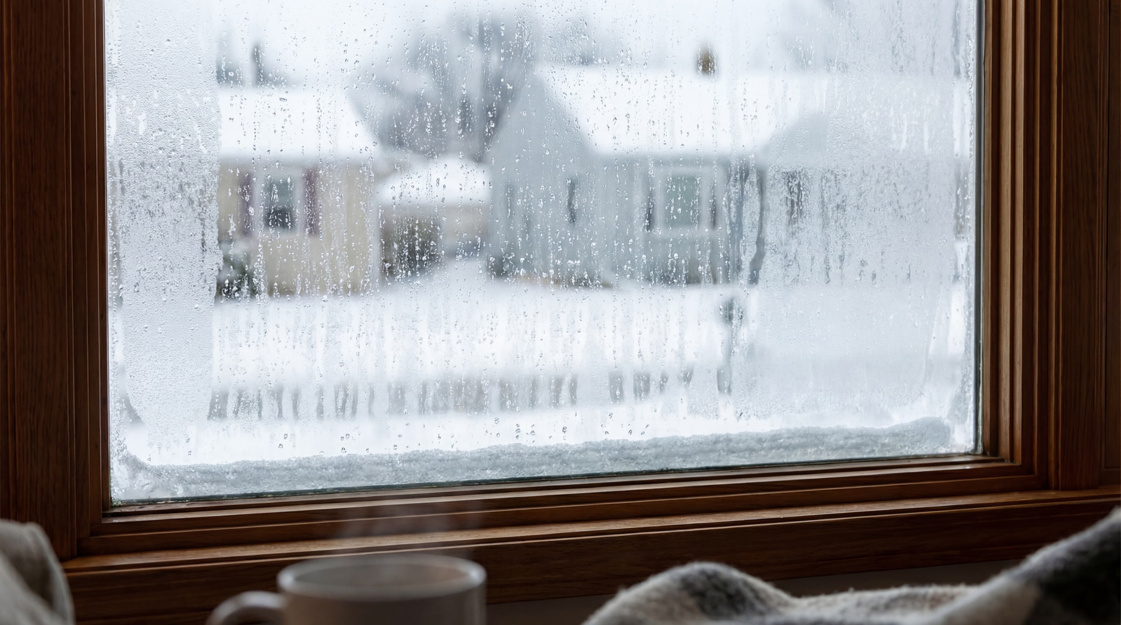 Window with condensation and snow-covered houses outside.