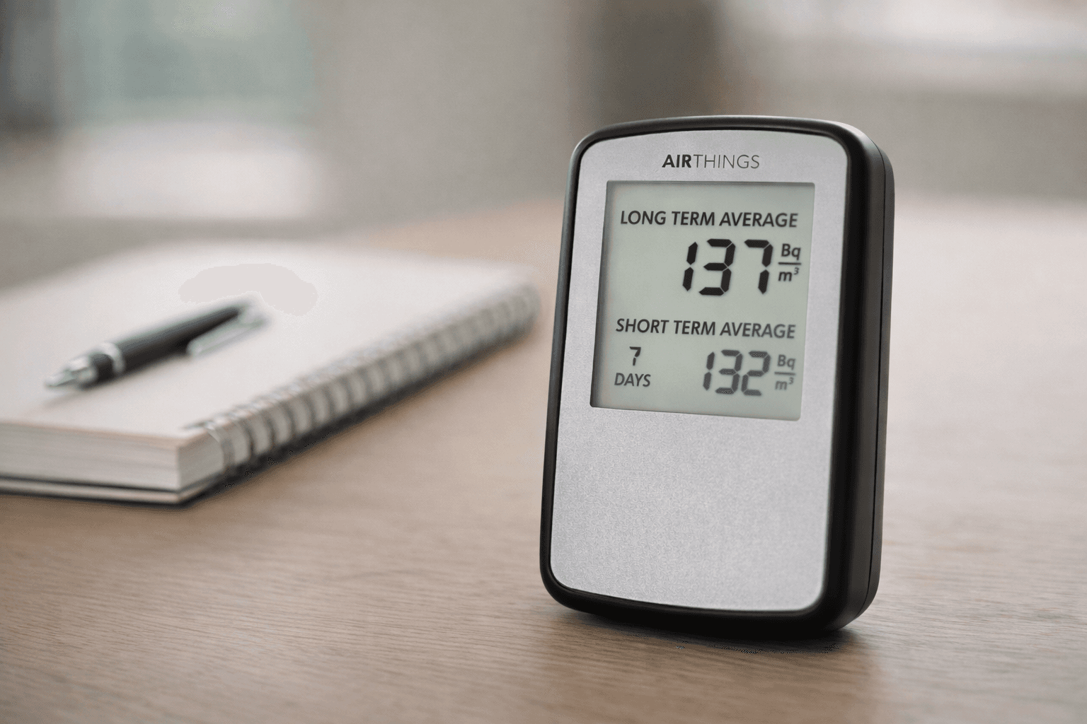 Digital radon detector with readings on a wooden desk.