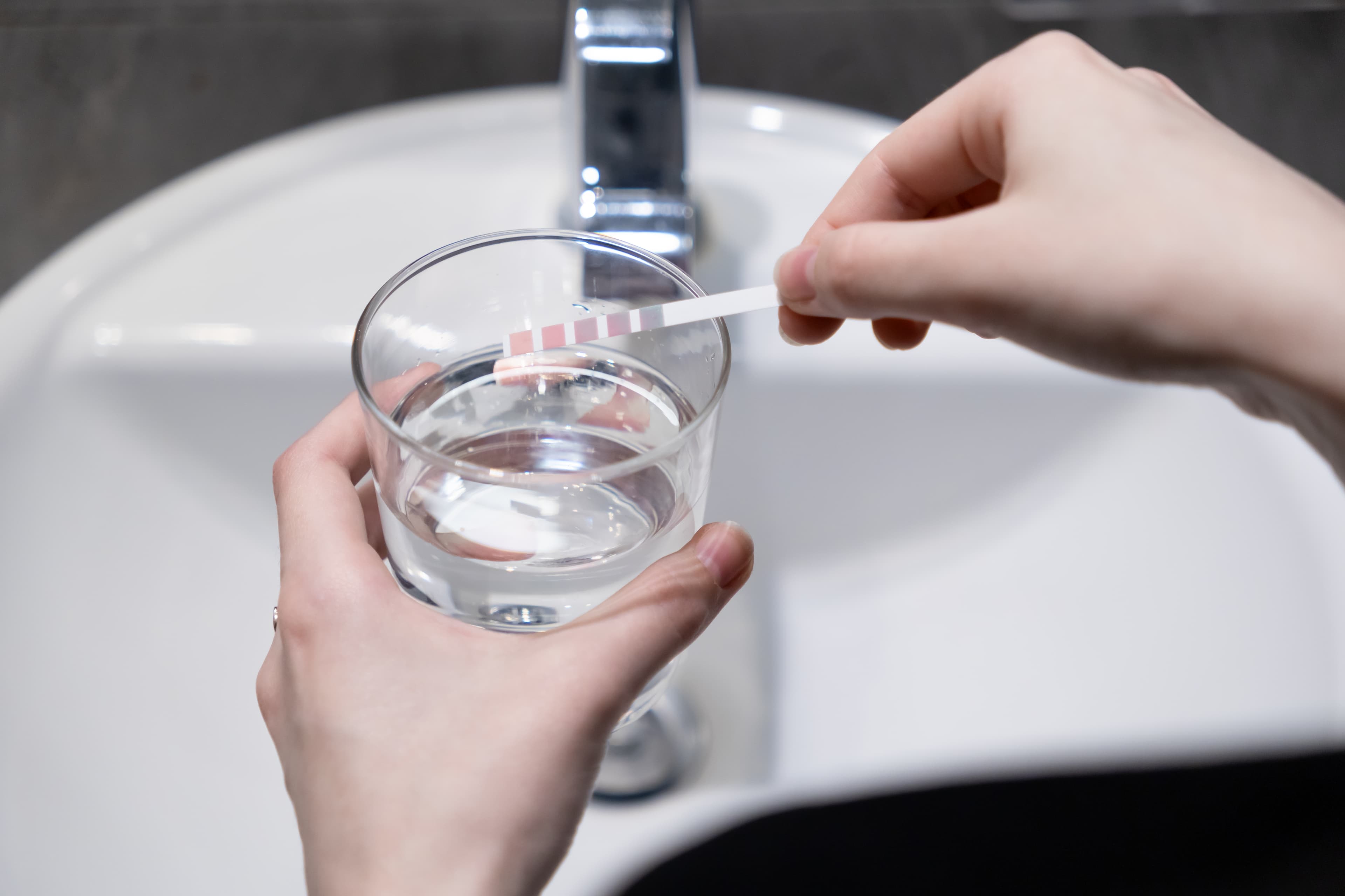 Person testing well water with pH strip over a sink.